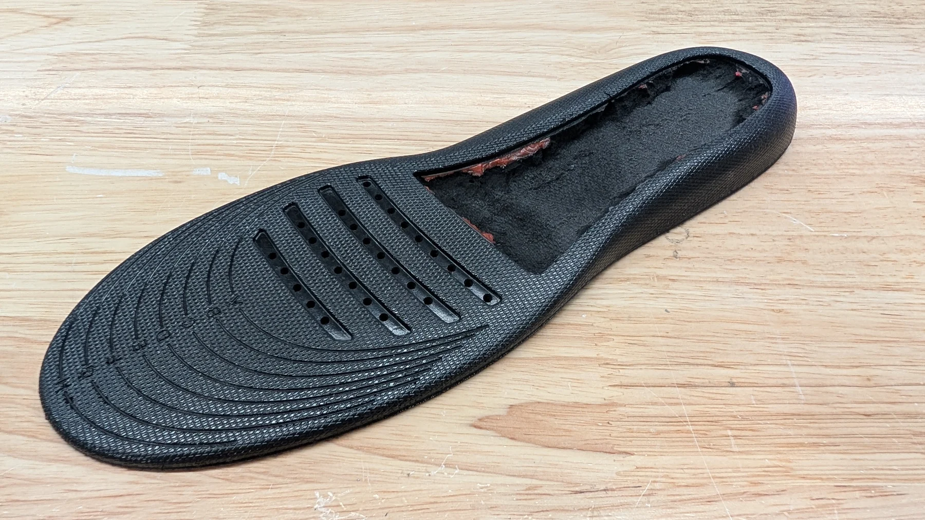 Black 3D printed insole housing with a slotted forefoot on a wooden surface